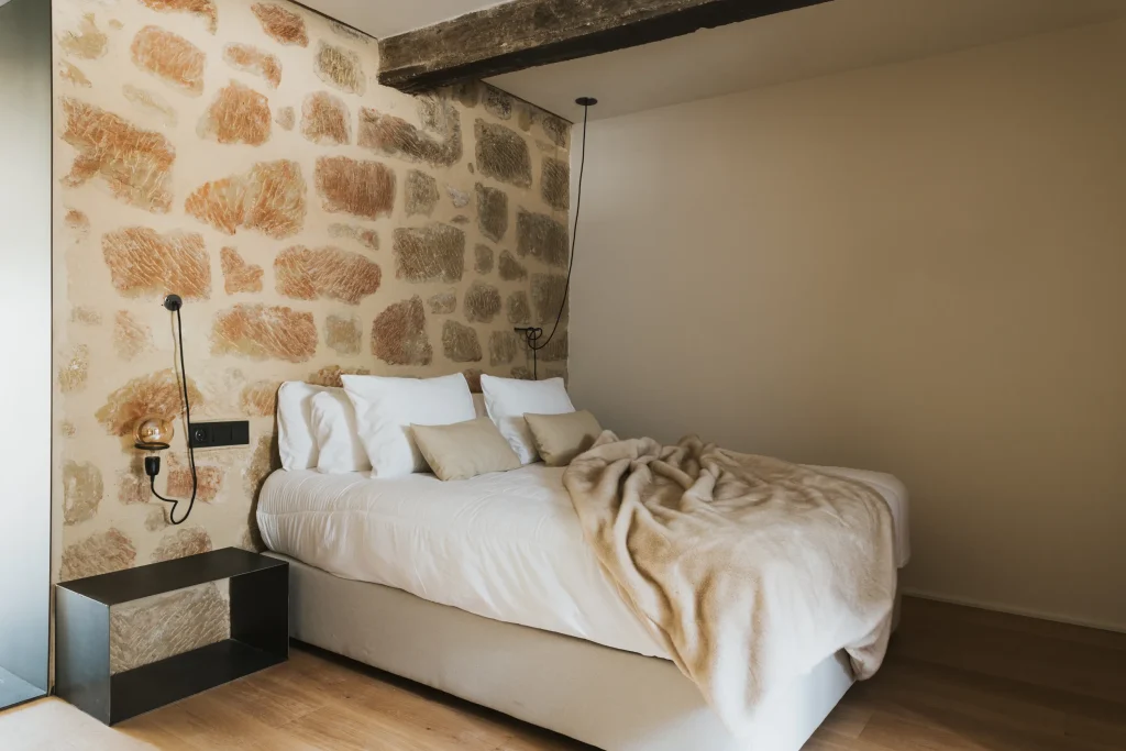 Dormitorio del apartamento 5 con cabecero de piedra y ropa de cama blanca.