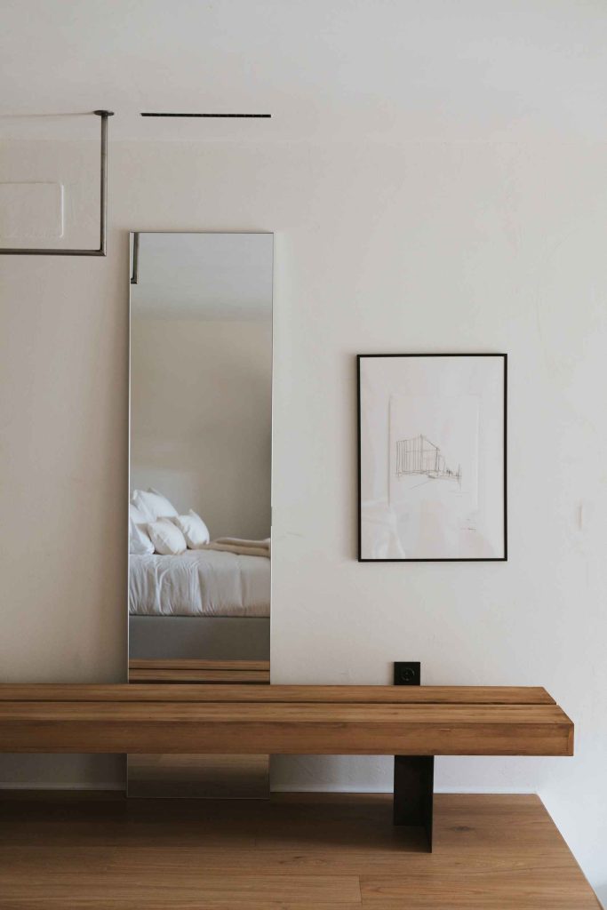 Vestidor abierto del apartamento 2 con lámina enmarcada, espejo y banco de madera.