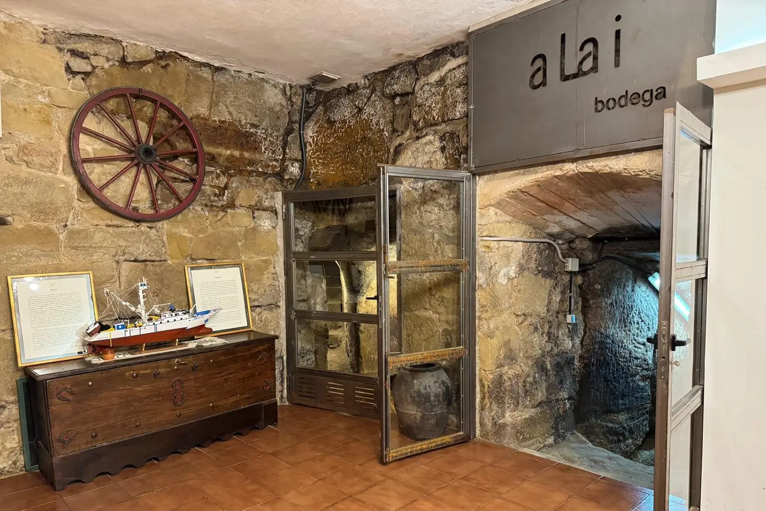 Interior del calado histórico de Los Ojos del Alai, con muros de piedra y utensilios tradicionales de bodega.